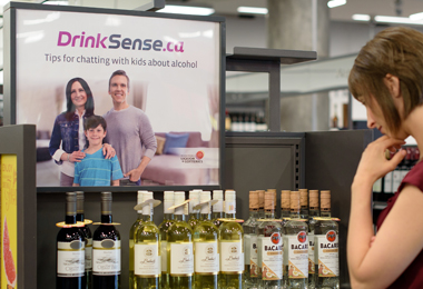 DrinkSense poster beside a woman choosing a bottle of wine.